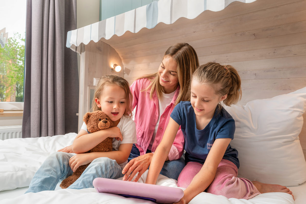 Mutter mit zwei Kindern im Hotelzimmer auf dem Bett – entspannte Familiensituation
