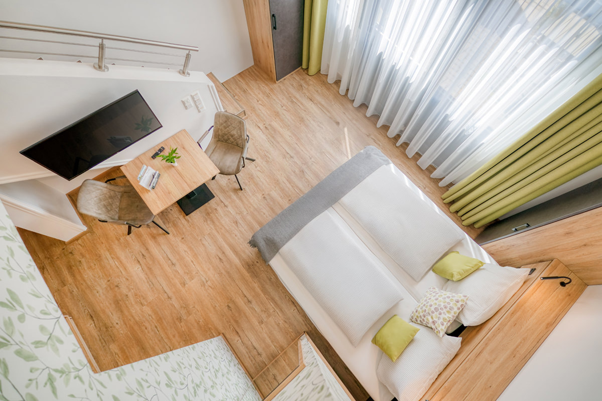 Hotelzimmer aus der Vogelperspektive mit Doppelbett, Schreibtisch und großer Fensterfront